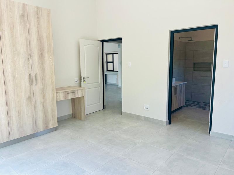 A modern, neutral bedroom featuring built-in cabinetry, tiled flooring, and direct access to an en-suite bathroom.
