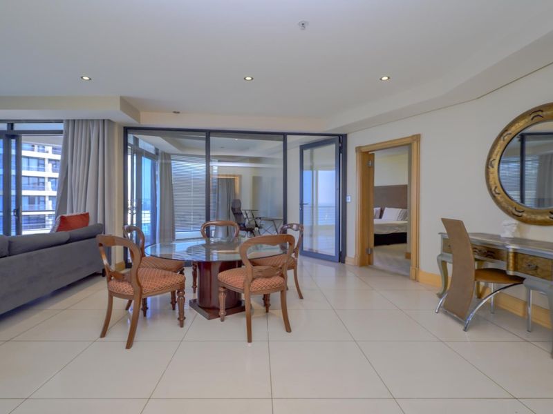 Spacious open-plan living and dining area featuring large format floor tiles, recessed lighting, and seamless access to an enclosed balcony through sliding glass doors.