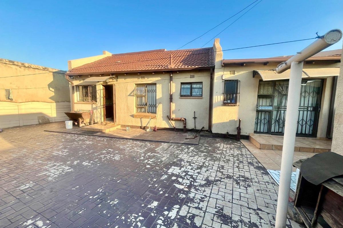 Rear exterior view of the house featuring a paved courtyard, tiled roof, and security-fitted windows and doors.