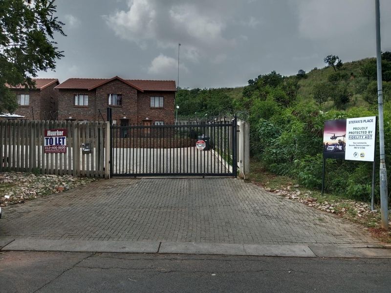 Front view of a brick apartment complex featuring a paved driveway, secure gated entrance, and perimeter fencing with security measures.