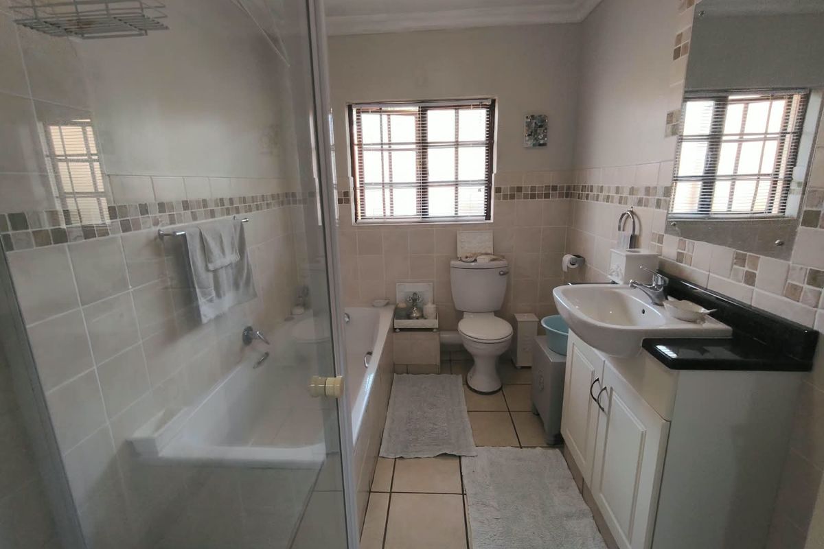 A functional bathroom featuring a bathtub, separate glass-enclosed shower, vanity with basin, and neutral wall and floor tiling.