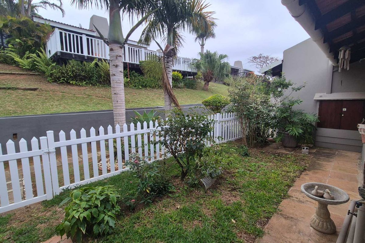 A rear garden area featuring a white picket fence, paved patio space, and established landscaping with views of neighboring townhouse units.