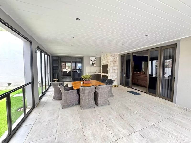 Spacious covered patio featuring large format floor tiles, recessed lighting, a built-in braai with stone cladding, and seamless access to the interior living areas.