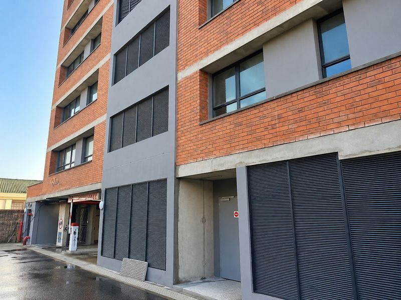 Exterior view of a modern apartment building featuring a red brick facade, grey concrete accents, and dark metal louvre screening.