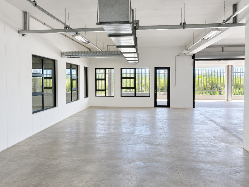 A spacious, modern industrial open-plan area featuring polished concrete floors, exposed ventilation ductwork, and large windows with security bars, offering a clean, versatile workspace.