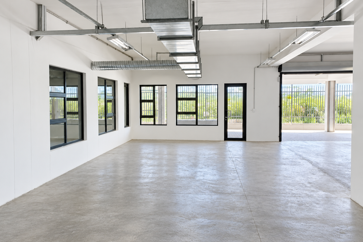A spacious, modern industrial open-plan area featuring polished concrete floors, exposed ventilation ductwork, and large windows with security bars, offering a clean, versatile workspace.