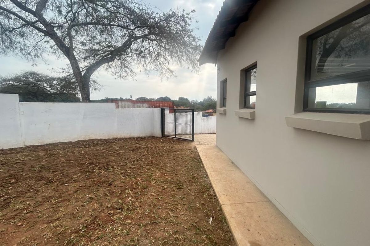 A view of the side exterior of the house featuring a paved walkway, perimeter boundary wall, and an open garden area.
