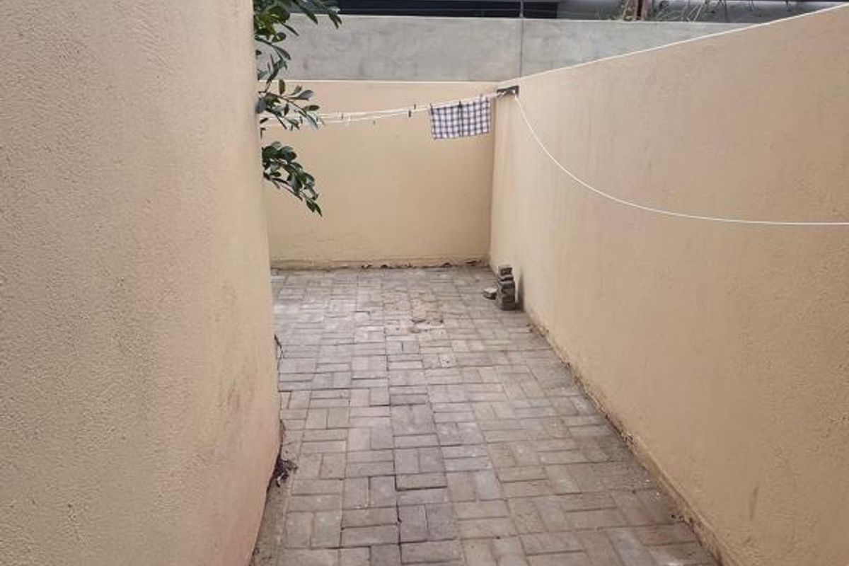 A narrow paved side courtyard area enclosed by boundary walls, featuring a simple utility space for outdoor drying.