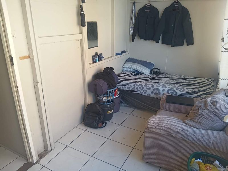 A compact bedroom featuring tiled flooring and a built-in wall niche, currently showing signs of wear and requiring cosmetic updates.