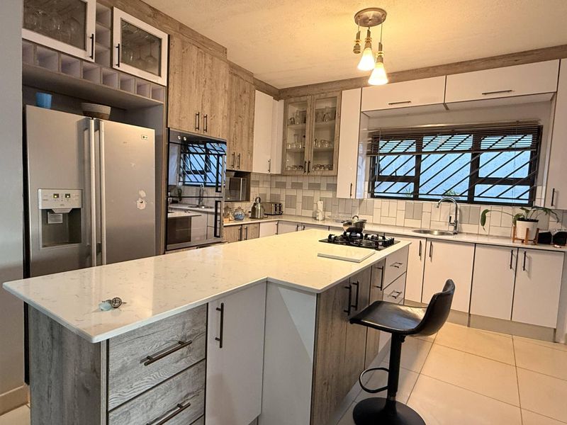 Modern kitchen featuring a central island with quartz countertops, gas hob, ample built-in cabinetry, and a tiled backsplash with integrated sink.