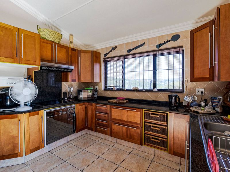 A functional kitchen featuring warm-toned wooden cabinetry, dark granite countertops, built-in oven, extractor fan, and tiled flooring with a window overlooking the exterior.