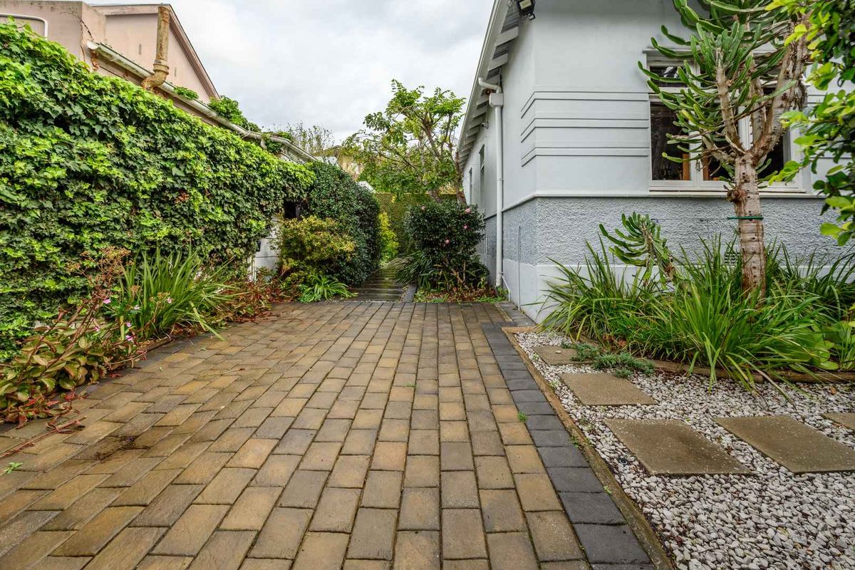A paved side walkway featuring established garden beds, climbing ivy on the boundary wall, and stone stepping stones set in gravel.