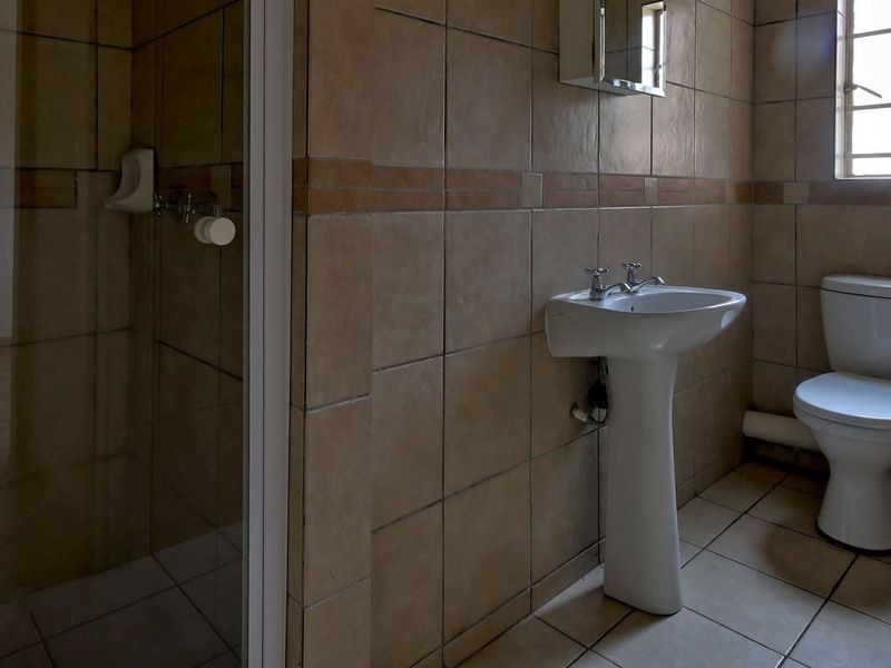 A functional bathroom featuring a pedestal basin, toilet, and a separate shower enclosure with neutral wall and floor tiling.
