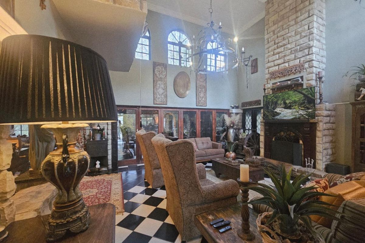 Spacious living room featuring a double-volume ceiling, a prominent stone-clad fireplace, arched windows, and classic black and white checkered flooring.