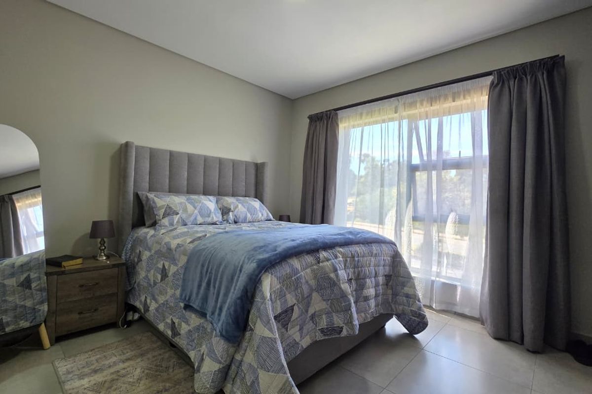 A well-maintained bedroom featuring neutral wall tones, tiled flooring, and a large window with curtains, providing ample natural light.