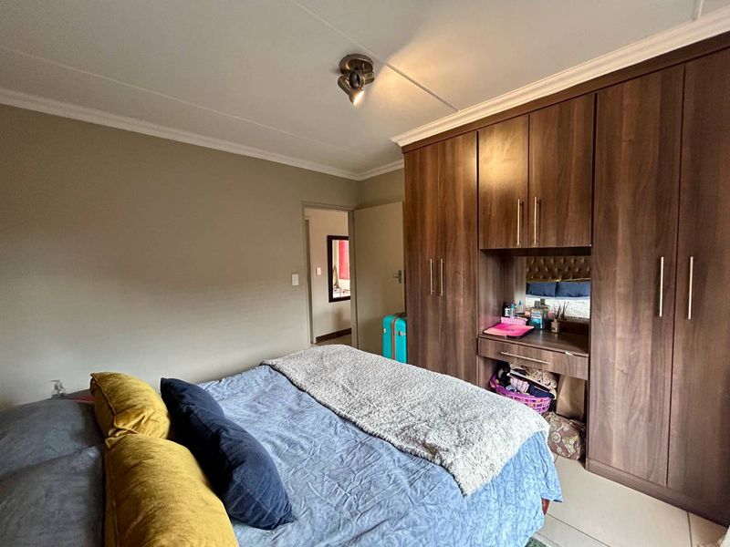 A bedroom featuring dark wood built-in cupboards with an integrated vanity area, tiled flooring, and neutral wall finishes.