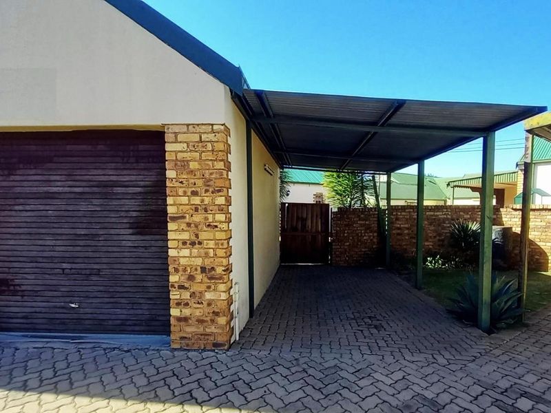 A single garage with a roller door and an adjacent covered carport, featuring brick paving and a secure boundary wall.