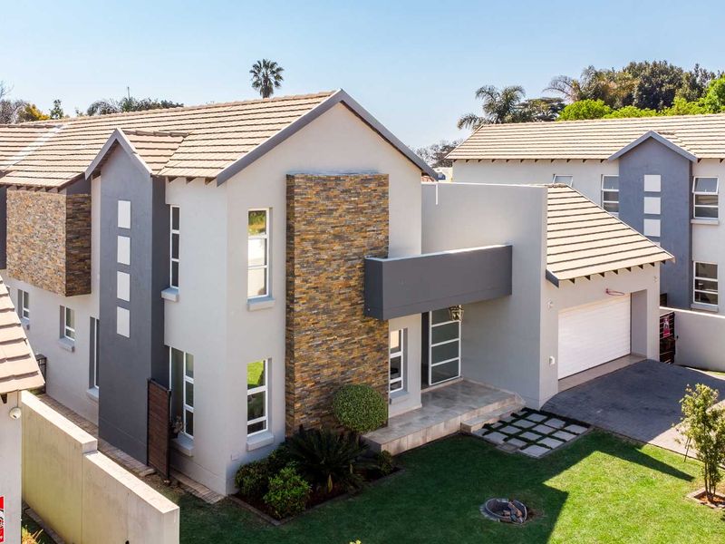 Modern double-storey residential property featuring stone cladding accents, a tiled roof, double garage, and a well-maintained front garden with paved driveway.