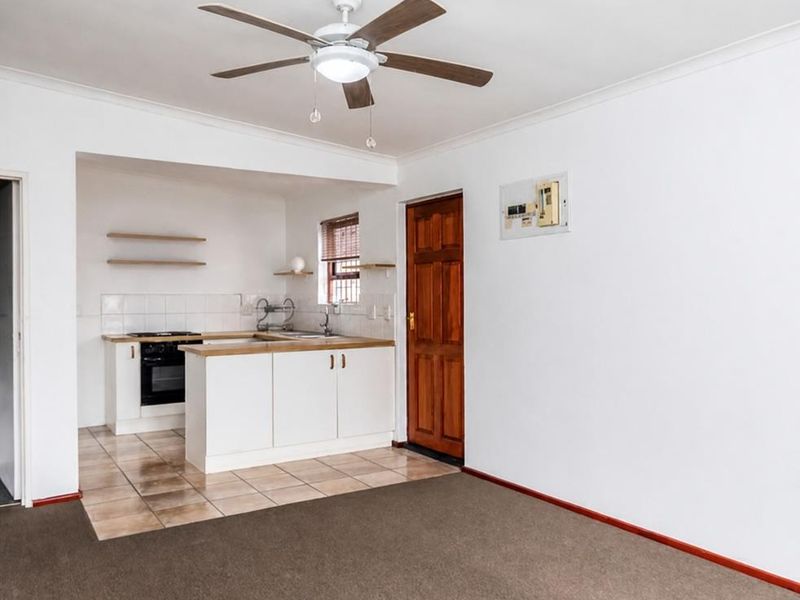 An open-plan living area featuring a compact kitchen with built-in cabinetry, oven, and hob, transitioning from tiled kitchen flooring to carpeted living space.