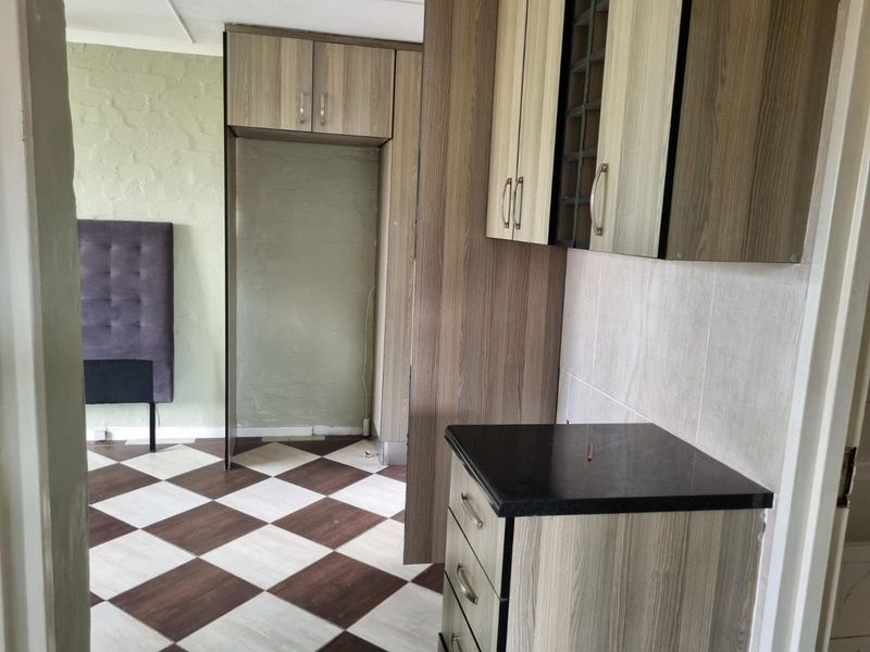 A compact kitchen area featuring wood-look cabinetry, dark countertops, and a checkered tile floor, currently in need of finishing touches and updates.