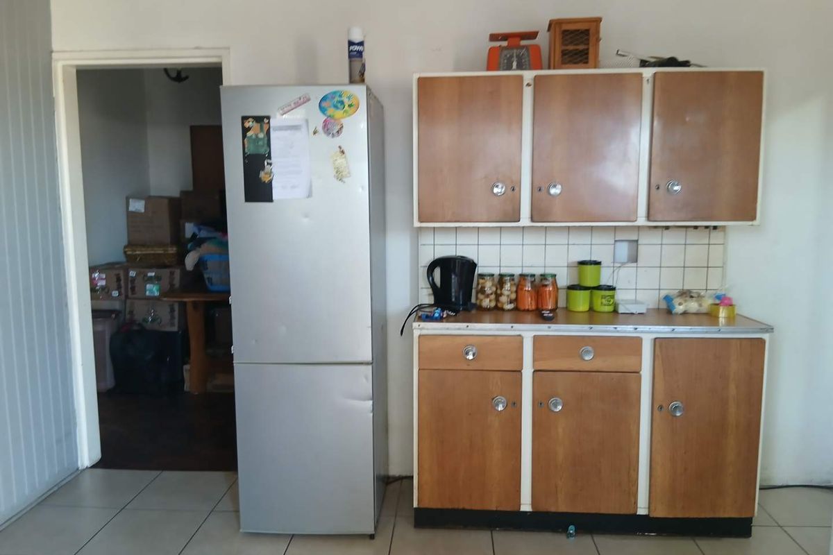 A compact kitchen area featuring dated wooden cabinetry, a tiled backsplash, and tiled flooring, providing a functional but basic preparation space.