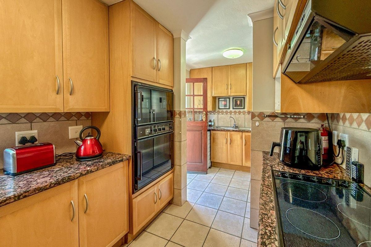 A functional kitchen featuring wooden cabinetry, granite countertops, a built-in oven, electric hob, and tiled flooring with a secondary prep area.