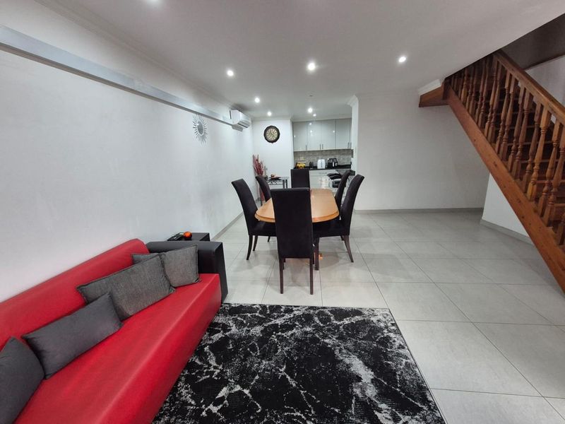 Open-plan living and dining area featuring tiled flooring, recessed lighting, and a wooden staircase, leading to a functional kitchen space.