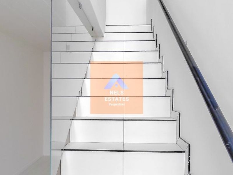 A bright, modern staircase featuring white tiled steps, a sleek glass balustrade, and a contrasting dark handrail leading to a timber-paneled ceiling.