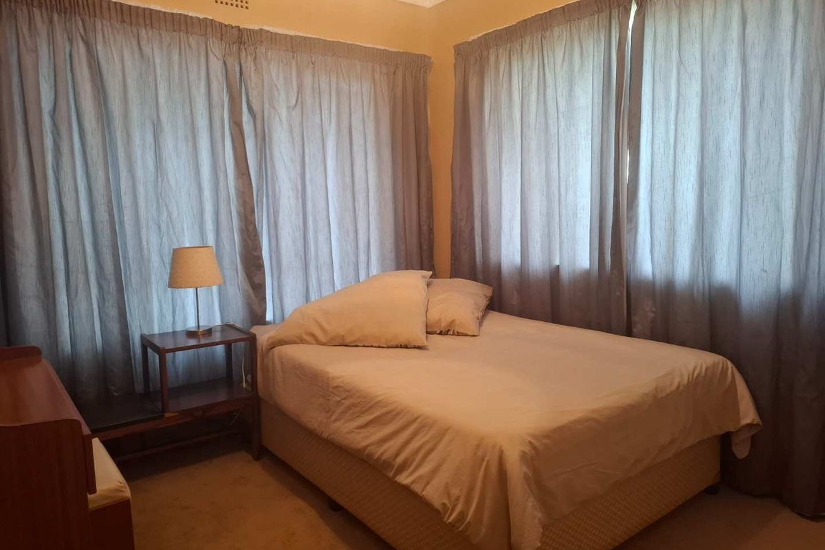 A bedroom featuring carpeted flooring and corner windows with curtains.