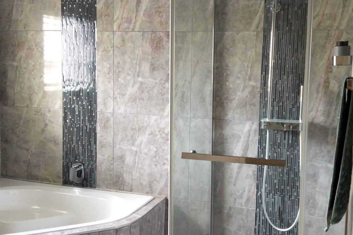 Modern bathroom featuring a corner bathtub, a glass-enclosed shower, and contemporary grey marble-effect wall tiling with decorative mosaic accents.