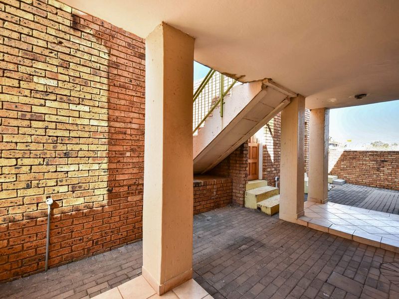 A covered outdoor rear area featuring brick construction, concrete support pillars, and an external staircase leading to the upper level.
