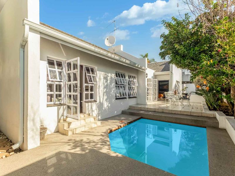 Rear exterior view featuring a swimming pool, tiled patio area, and white facade with multiple casement windows and french door access.