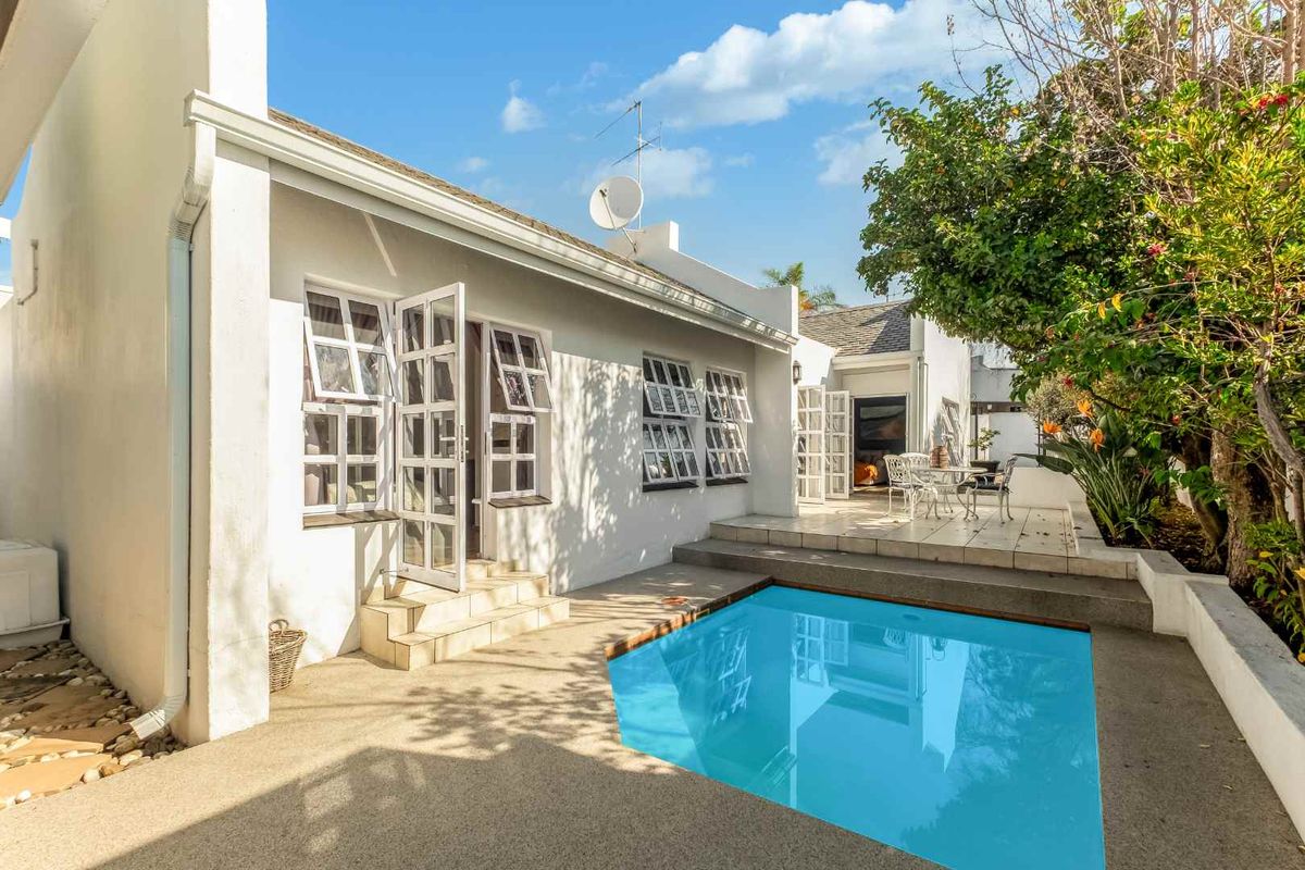 Rear exterior view featuring a swimming pool, tiled patio area, and white facade with multiple casement windows and french door access.