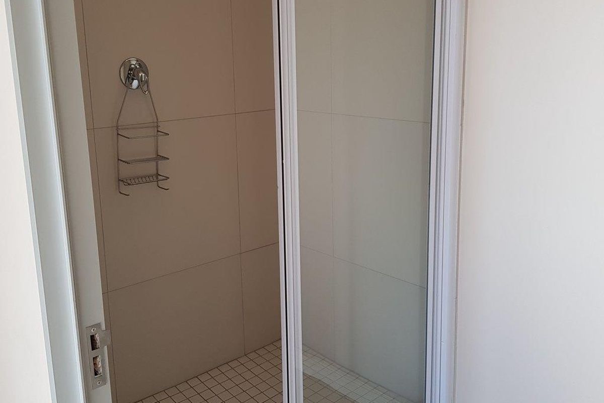 A clean, functional shower stall featuring neutral wall tiling, a glass door, and a built-in shower mixer.
