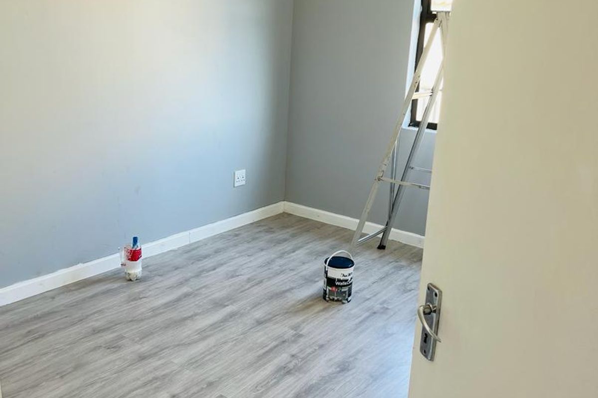 A clean, empty bedroom featuring modern grey laminate flooring and neutral painted walls, ready for personalization.