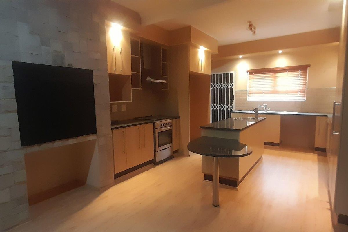 Spacious kitchen featuring modern cabinetry, stone countertops, a central island with breakfast bar, and a distinctive stone feature wall with integrated lighting.