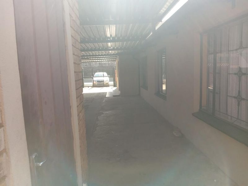 A covered outdoor walkway or carport area featuring concrete flooring, brick walls, and security bars on the windows.