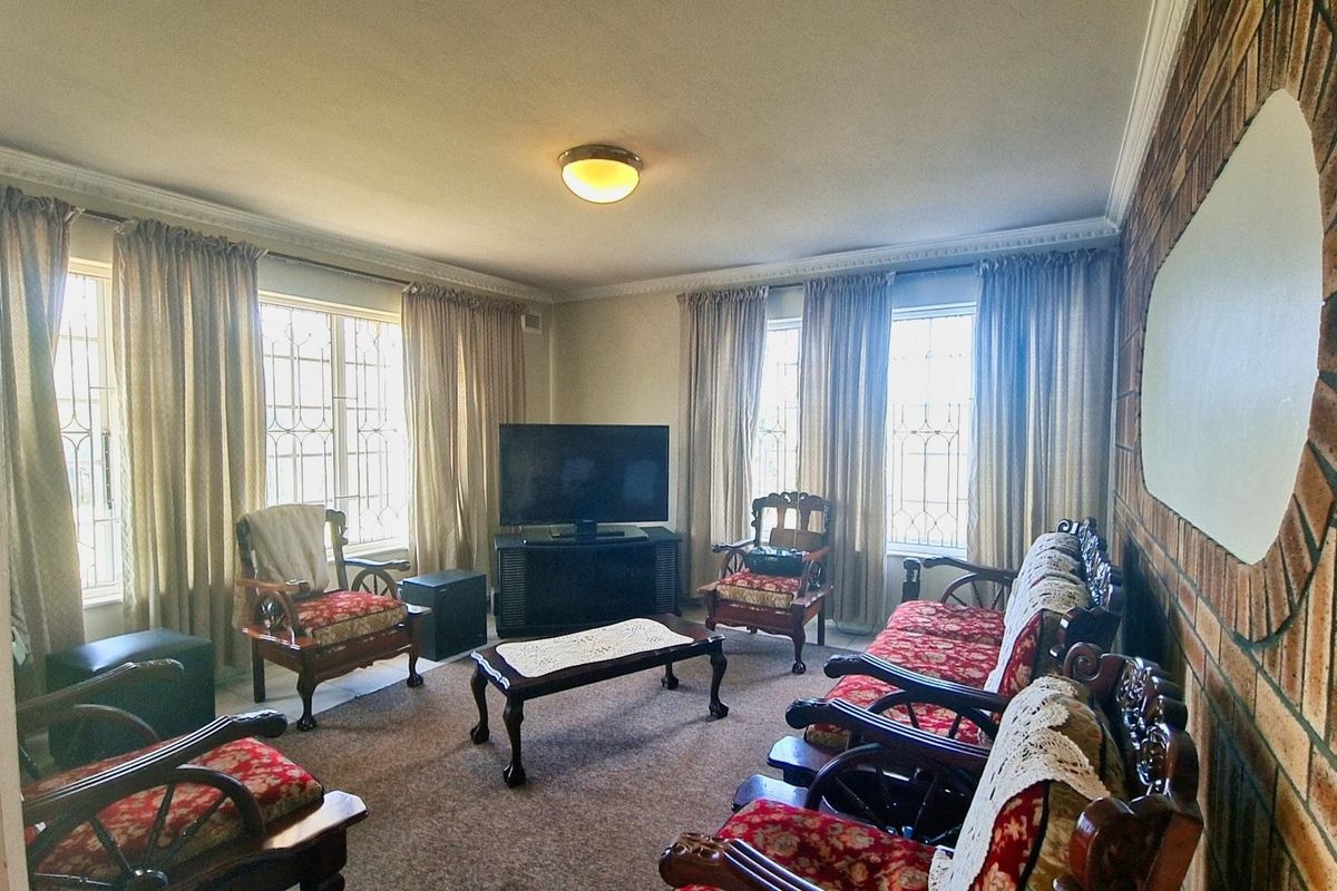 A living room featuring a brick accent wall, ceiling cornicing, and large windows with security bars, offering a traditional layout.