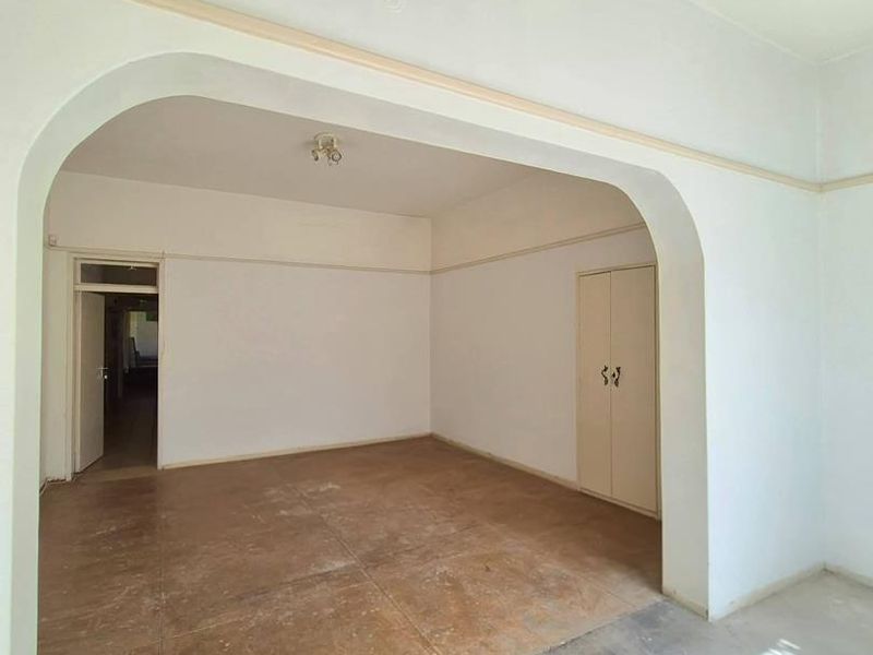 An empty living area featuring an arched transition, built-in storage, and tiled flooring, presenting a blank canvas for renovation.