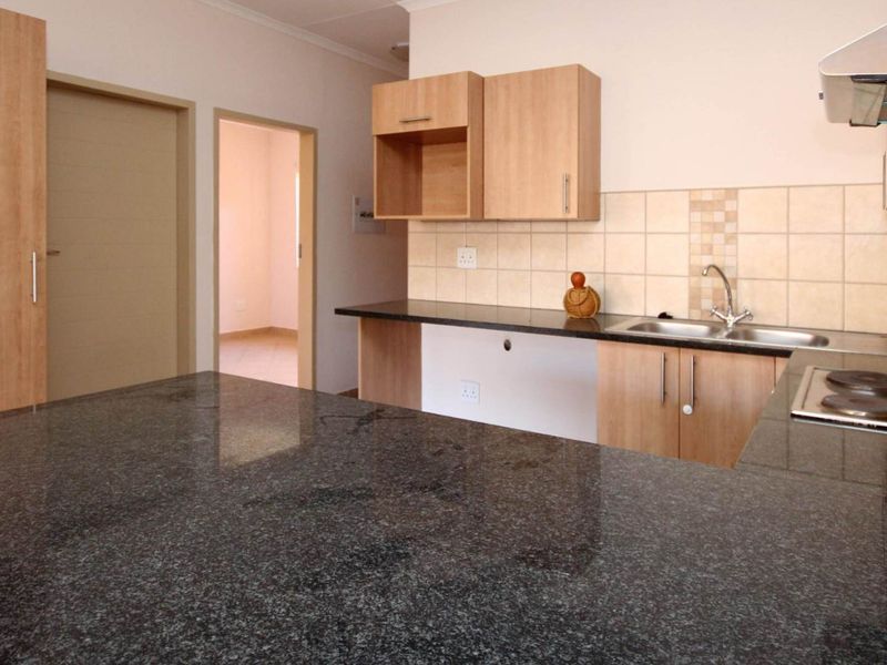 A functional kitchen featuring granite countertops, built-in wooden cabinetry, a stainless steel sink, and an integrated electric hob with an extractor fan.