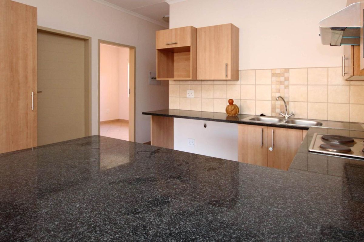 A functional kitchen featuring granite countertops, built-in wooden cabinetry, a stainless steel sink, and an integrated electric hob with an extractor fan.