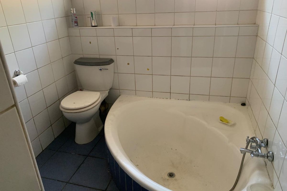 A compact bathroom featuring a corner bathtub, wall-mounted toilet, and full-height wall tiling.