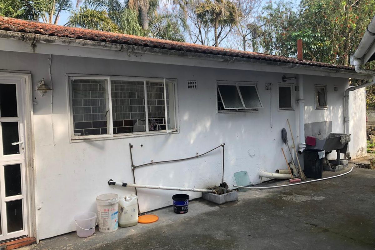 Rear exterior view of the property featuring a concrete patio area, tiled roof, and external utility sink with visible wear to the exterior finishes.