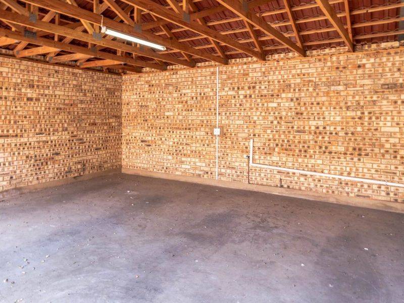 A spacious, functional garage featuring exposed brick walls, concrete flooring, and open timber roof trusses with overhead lighting.