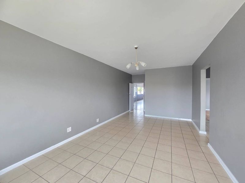 A spacious, empty living area featuring neutral grey walls and tiled flooring, offering a blank canvas for interior design and furniture placement.