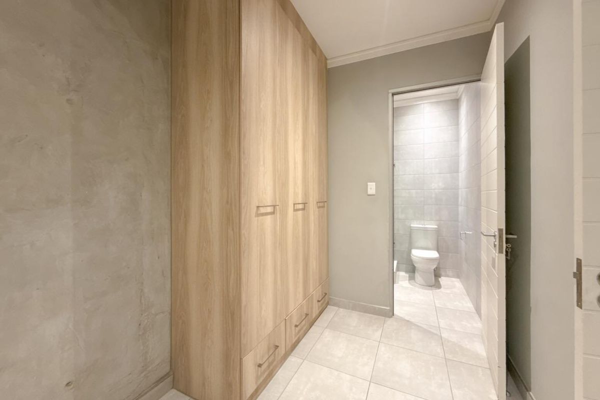 A modern bedroom area featuring light wood built-in wardrobes, tiled flooring, and an adjoining en-suite bathroom with a clean, contemporary finish.