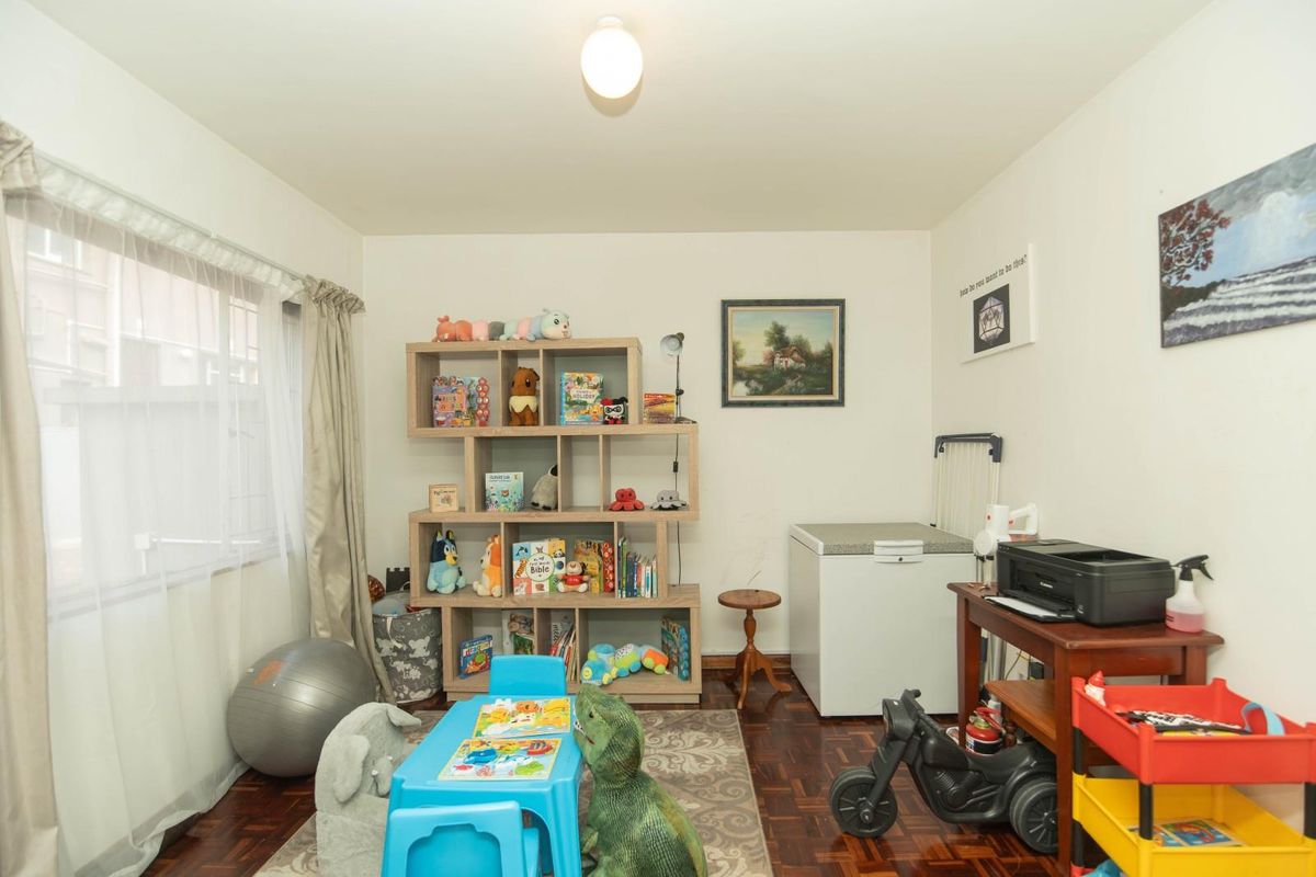 A versatile bedroom featuring classic parquet flooring and large windows, currently utilized as a multi-purpose play and utility space.