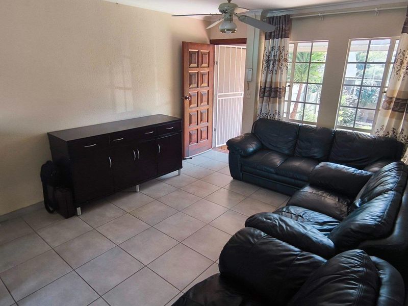A living room featuring tiled flooring, a ceiling fan, and natural light through large windows, with direct access to an exterior security gate.