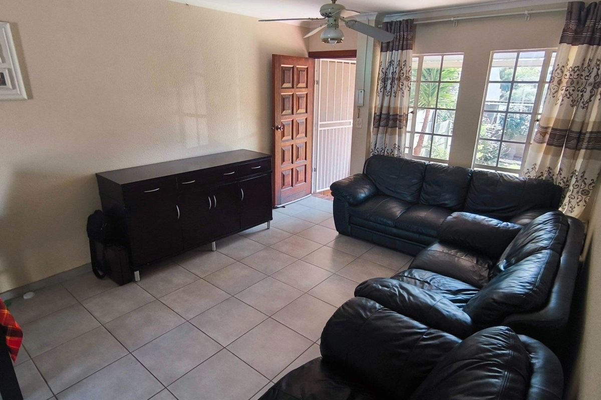 A living room featuring tiled flooring, a ceiling fan, and natural light through large windows, with direct access to an exterior security gate.