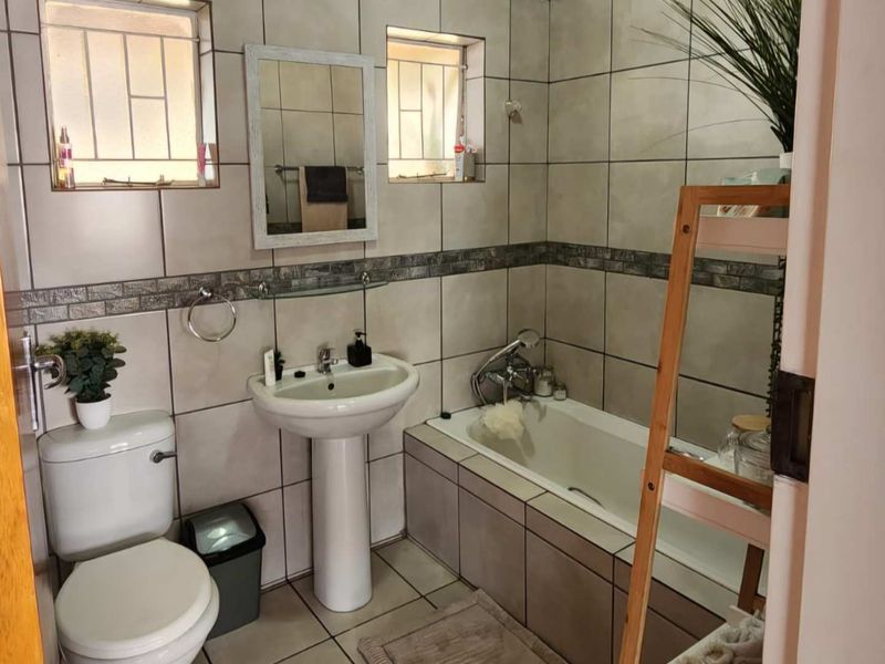 A functional bathroom featuring a pedestal basin, toilet, and bathtub with neutral wall and floor tiling.